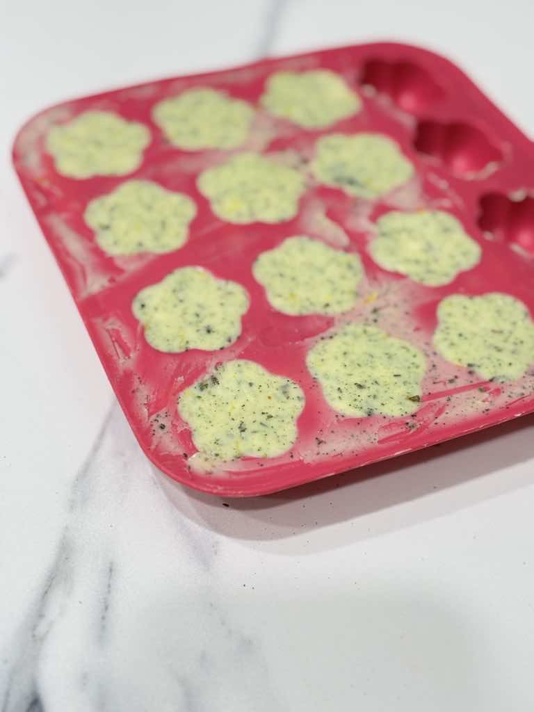 Soft herb butter mixture spooned into flower-shaped silicone molds, showcasing a traditional and simple German herb butter recipe using dried herbs.