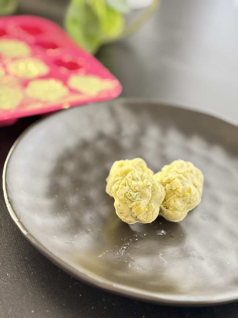 Two floral-shaped frozen herb butter pieces on a black plate, made from a nostalgic herb butter recipe with dried herbs.