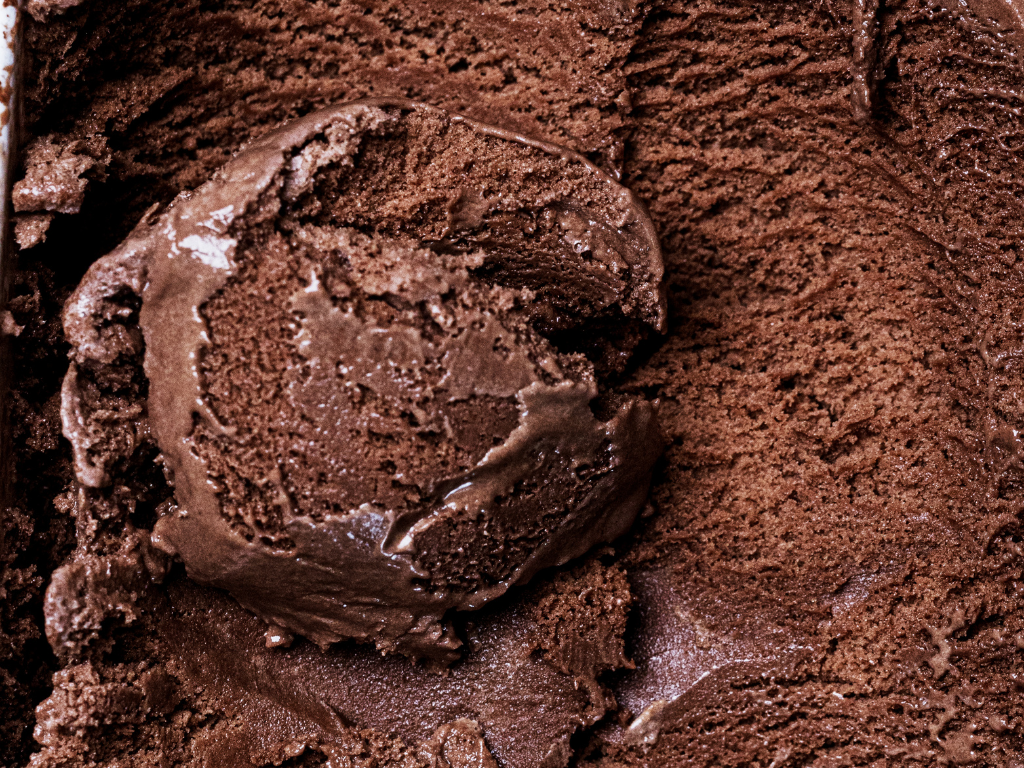 A close-up of rich, velvety homemade chocolate ice cream recipe without eggs, freshly scooped from the tub.