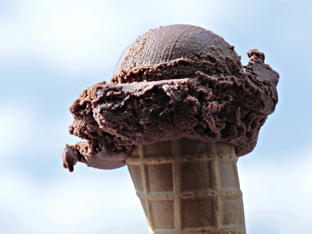 A scoop of smooth homemade chocolate ice cream recipe without eggs on a crisp waffle cone, held up to the sky.