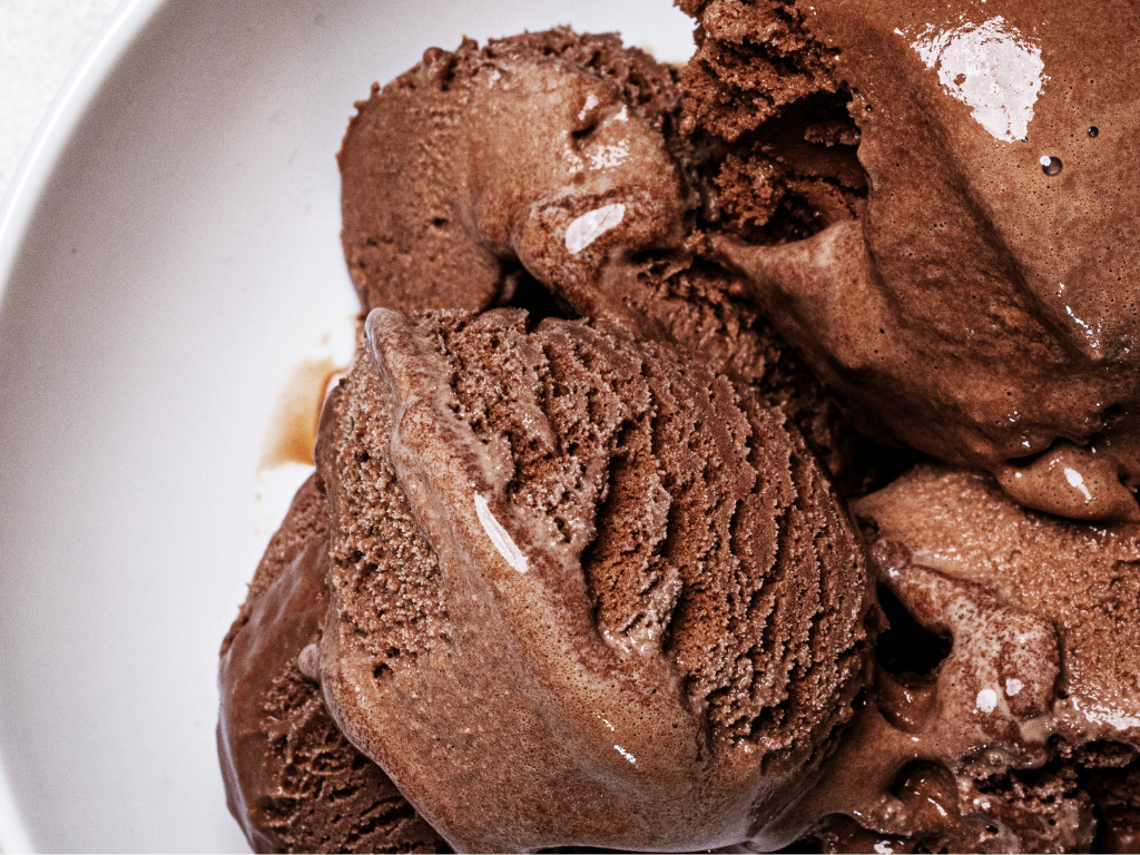 Melting scoops of homemade chocolate ice cream recipe without eggs in a bowl, showing its soft and creamy texture.