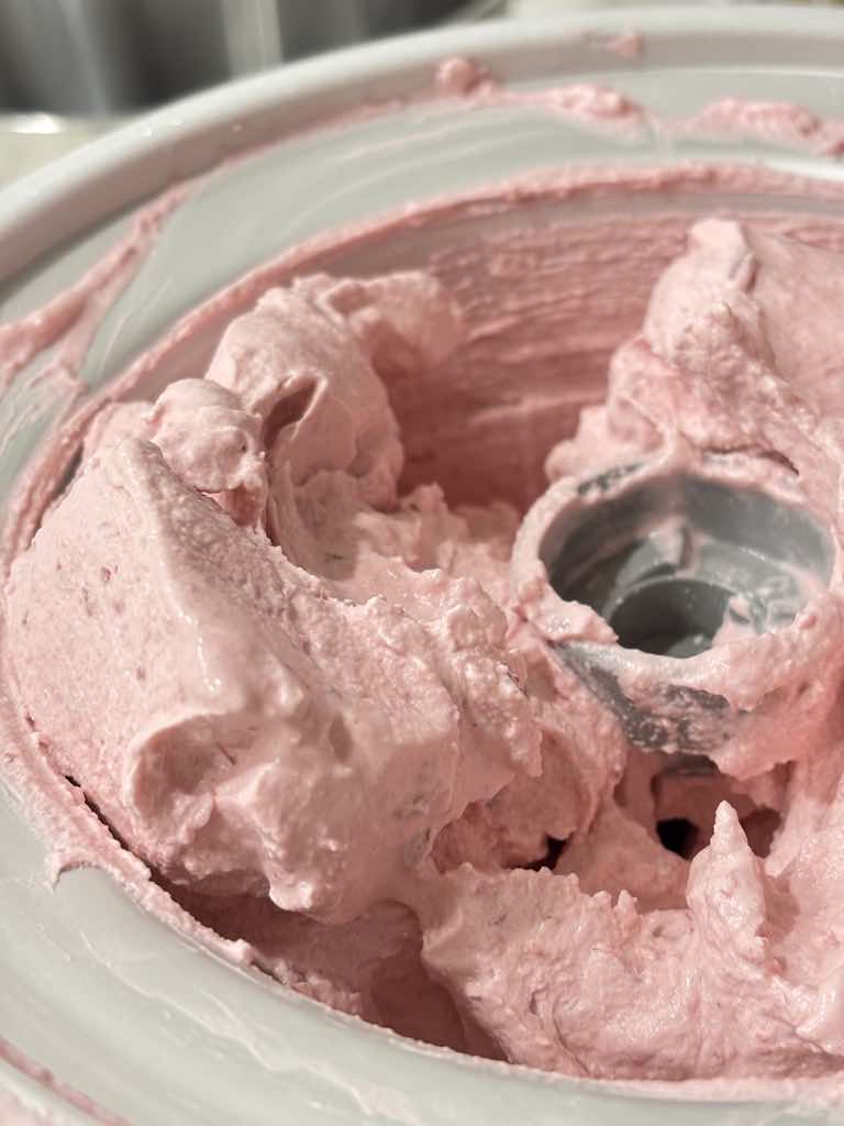 Smooth and creamy pink ice cream mixture churning in an ice cream maker, part of a homemade sour cherry ice cream recipe.