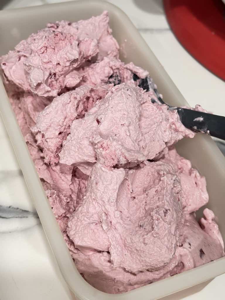 A container filled with fluffy pink homemade sour cherry ice cream, ready to freeze for later enjoyment.
