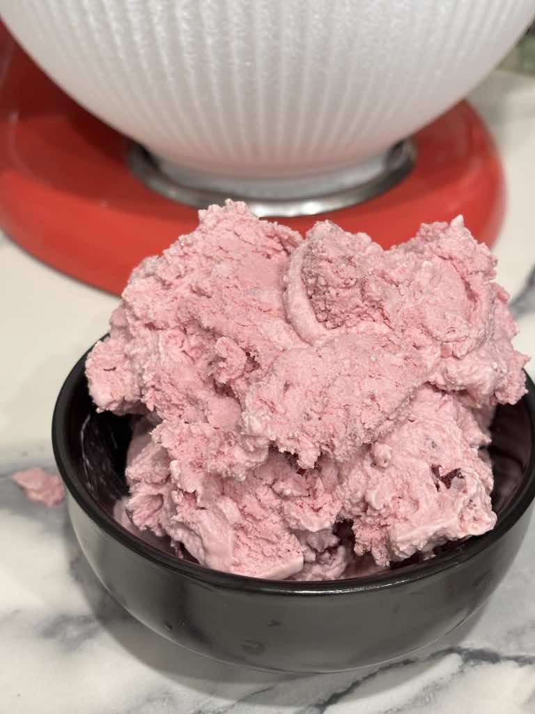A black bowl filled with freshly churned, creamy homemade sour cherry ice cream with a soft texture.