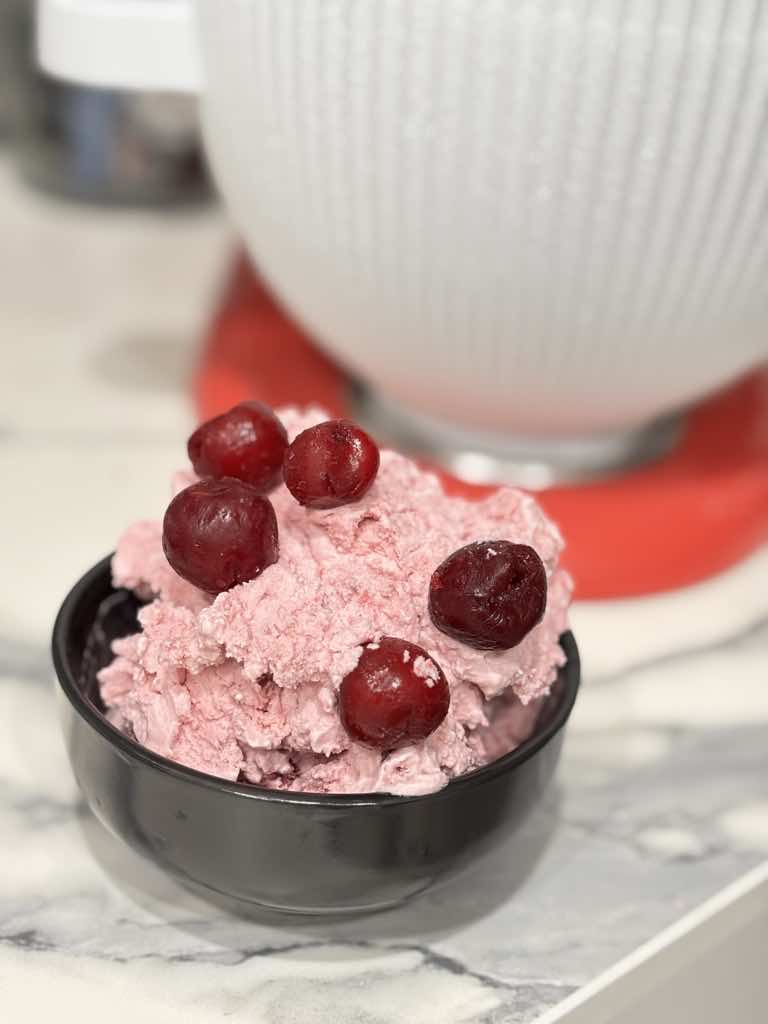 A black bowl with creamy homemade sour cherry ice cream, garnished with whole cherries on top.