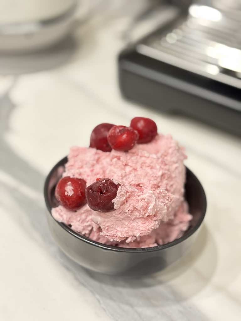 A close-up shot of a creamy pink scoop of homemade sour cherry ice cream topped with whole cherries.