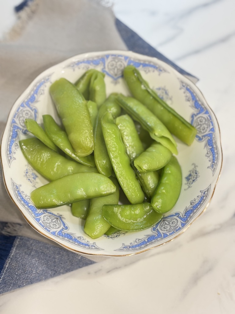 Steamed sugar snap peas served in a blue and white vintage bowl. A delicious result of learning how to steam sugar snap peas for a quick and healthy veggie snack.