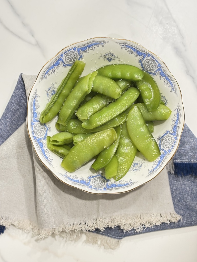 Top-down view of a bowl filled with freshly steamed sugar snap peas. A visual step in the process of how to steam sugar snap peas to preserve texture and flavor.