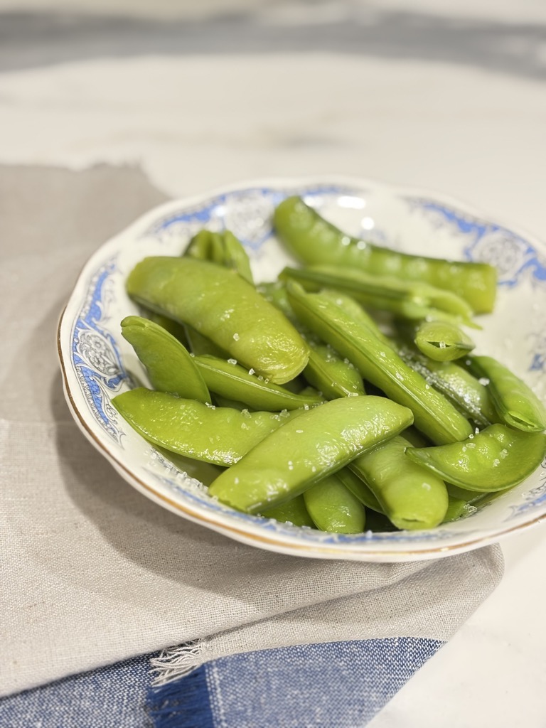 Steamed sugar snap peas in a patterned bowl on a napkin. Great texture captured for anyone wanting to learn how to steam sugar snap peas right.