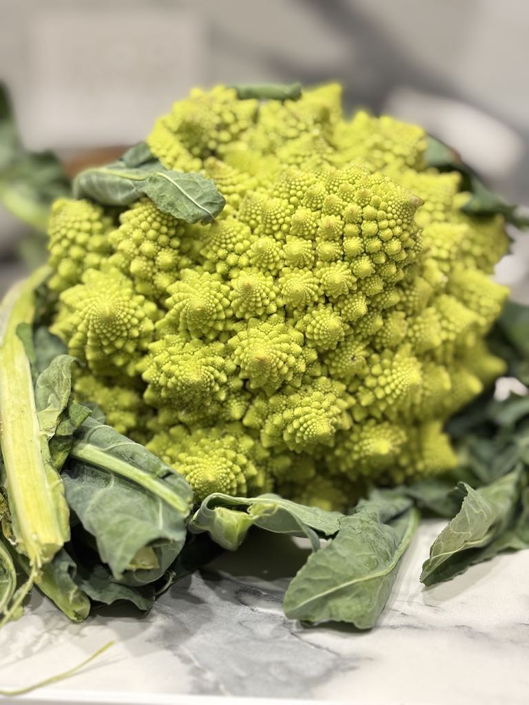 A head of vibrant Romanesco green cauliflower with its leaves still attached, ready to be used in a simple roasted green cauliflower recipe.