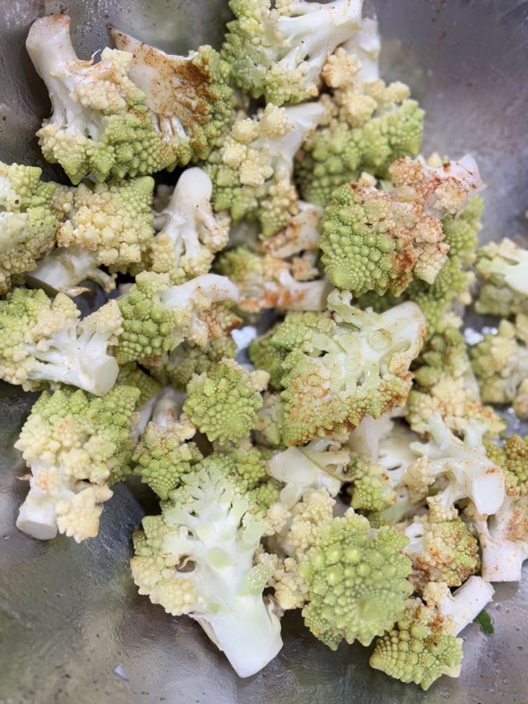 Fresh Romanesco green cauliflower florets sprinkled with paprika, salt, and olive oil in a bowl, the first step in this easy roasted green cauliflower recipe.