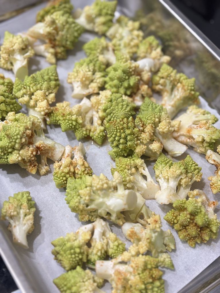 Chopped florets of green cauliflower spread evenly on a parchment-lined baking sheet, prepared for oven roasting in this simple green cauliflower recipe.