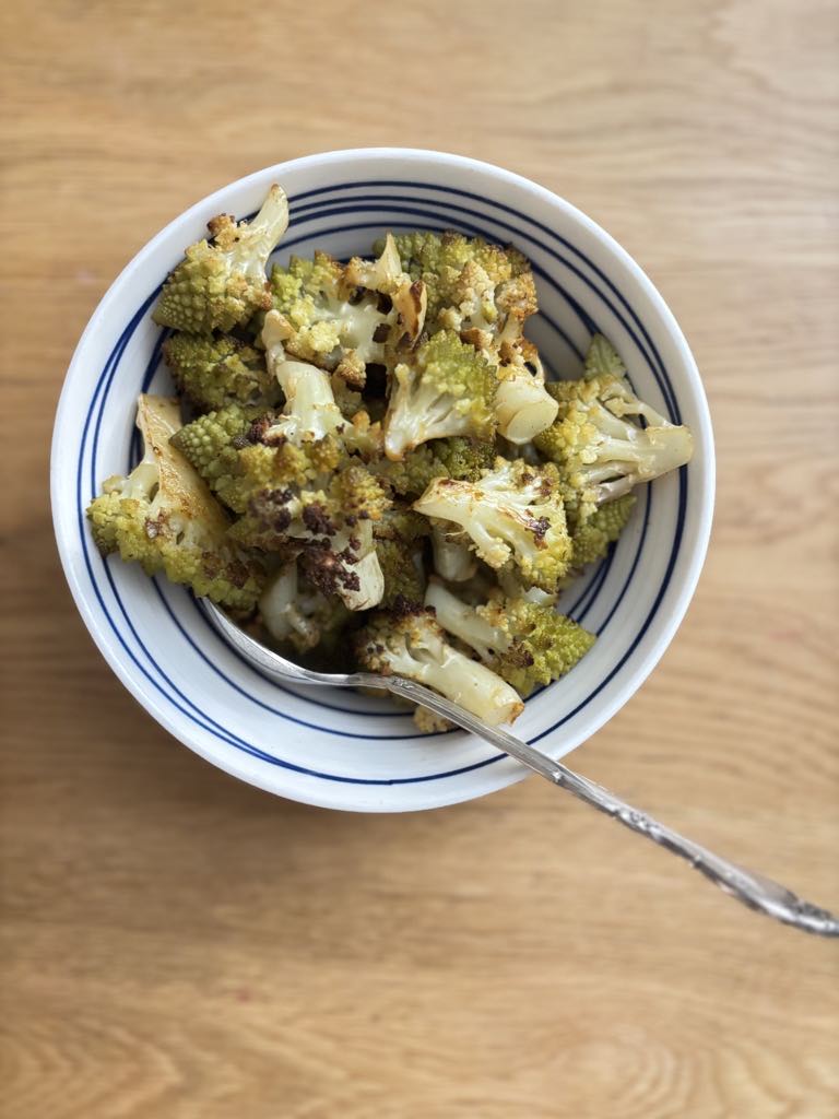 A close-up of roasted green cauliflower served in a simple striped bowl, highlighting the crispy, golden florets from this easy green cauliflower recipe.