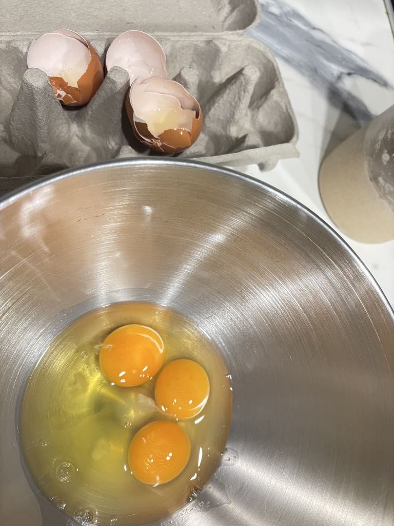 Fresh eggs cracked into a large mixing bowl, ready to be whisked with flour and milk for a traditional German pancake recipe.
