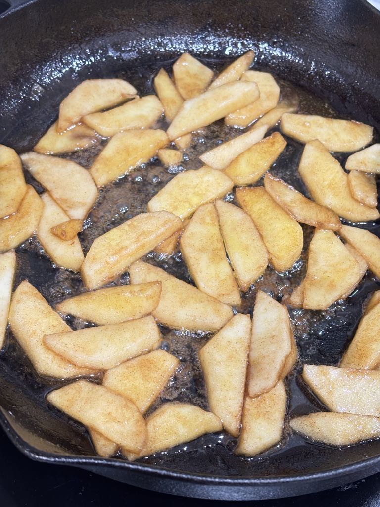 Caramelized apple slices bubbling in butter and sugar, creating a sweet, spiced filling for an oven-baked apple pancake.