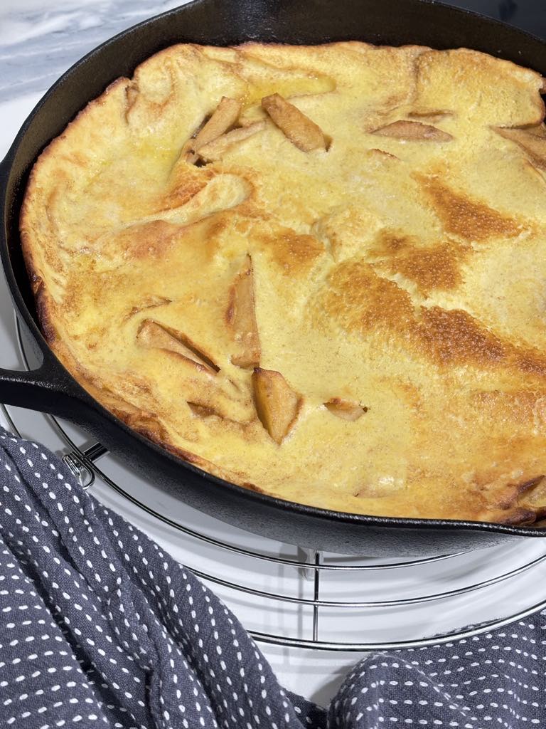 Freshly baked German-style apple pancake with puffed edges and golden crust, straight from the oven in a rustic cast iron skillet.
