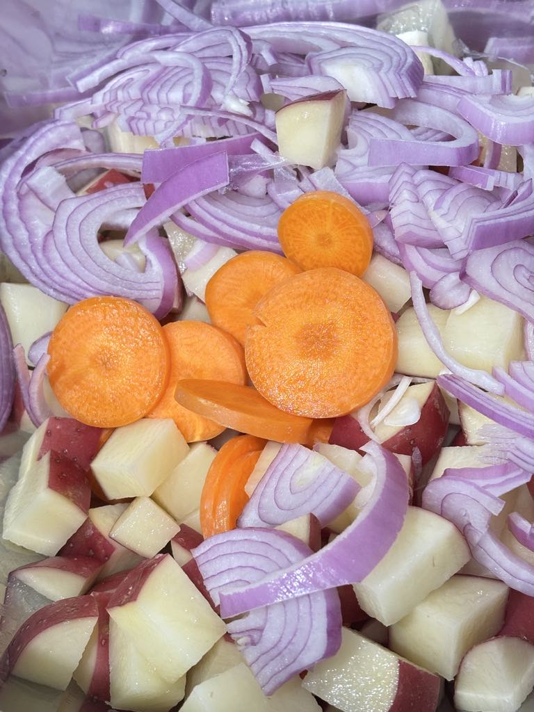 Diced red potatoes, sliced carrots, and thinly cut red onions piled in a mixing bowl, ready for seasoning in a simple potato carrot onion recipe.