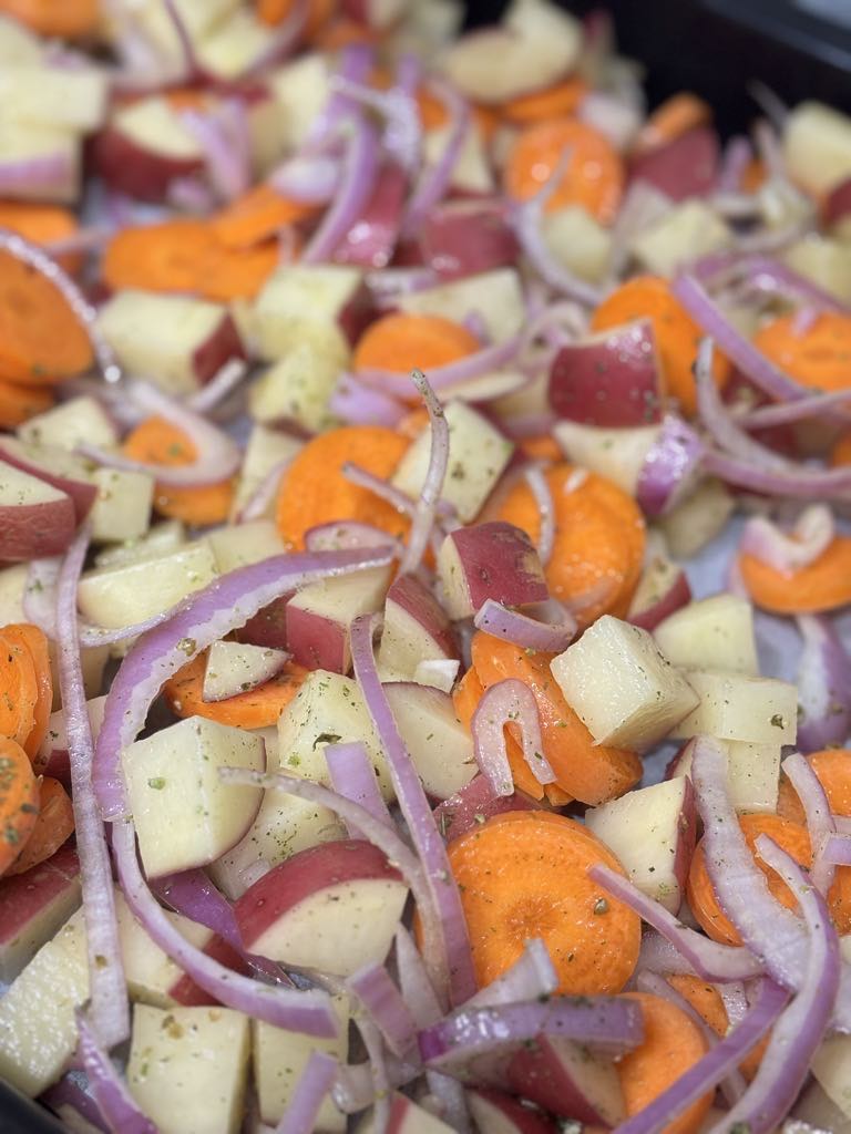 Sliced onions, carrots, and potato cubes on a lined sheet pan, tossed with oil and herbs, prepared for roasting into a cozy potato carrot onion sheet pan dinner.