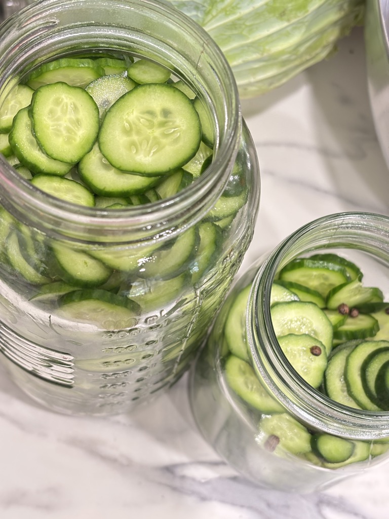 Close-up of cucumber slices in glass jars, waiting for the hot pickling brine in a simple, old-fashioned homemade dill pickles recipe.