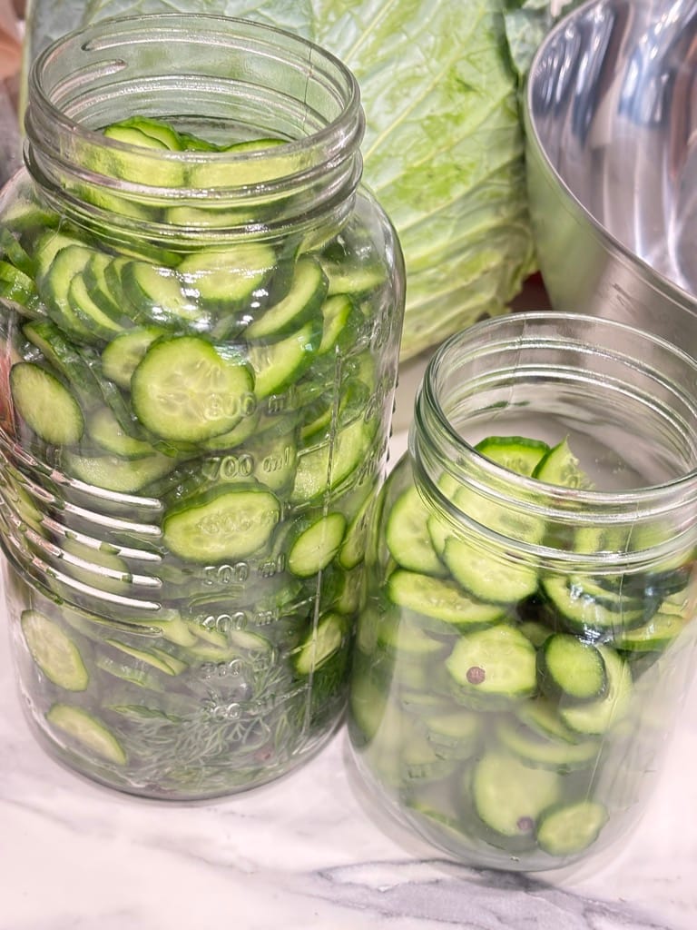 Two jars filled with sliced cucumbers and dill on a marble counter, showing the classic look of fresh refrigerator dill pickles made without canning.