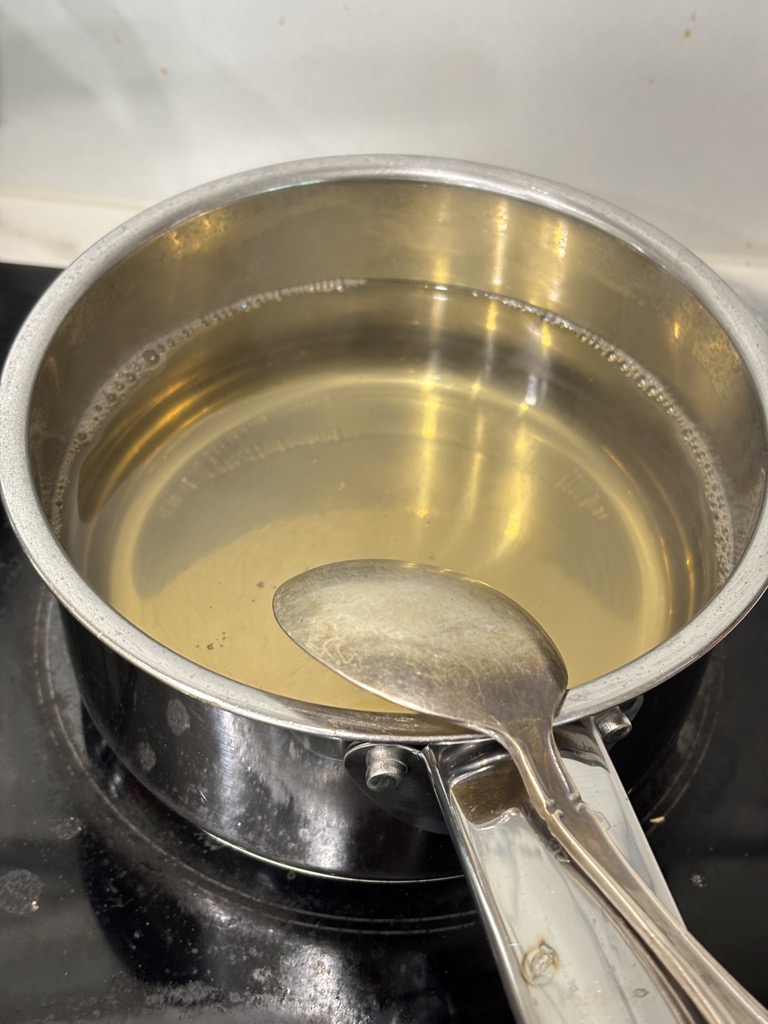 Silver saucepan filled with simmering pickling brine made from vinegar, salt, and sugar—the key to crisp, tangy homemade pickles without canning.