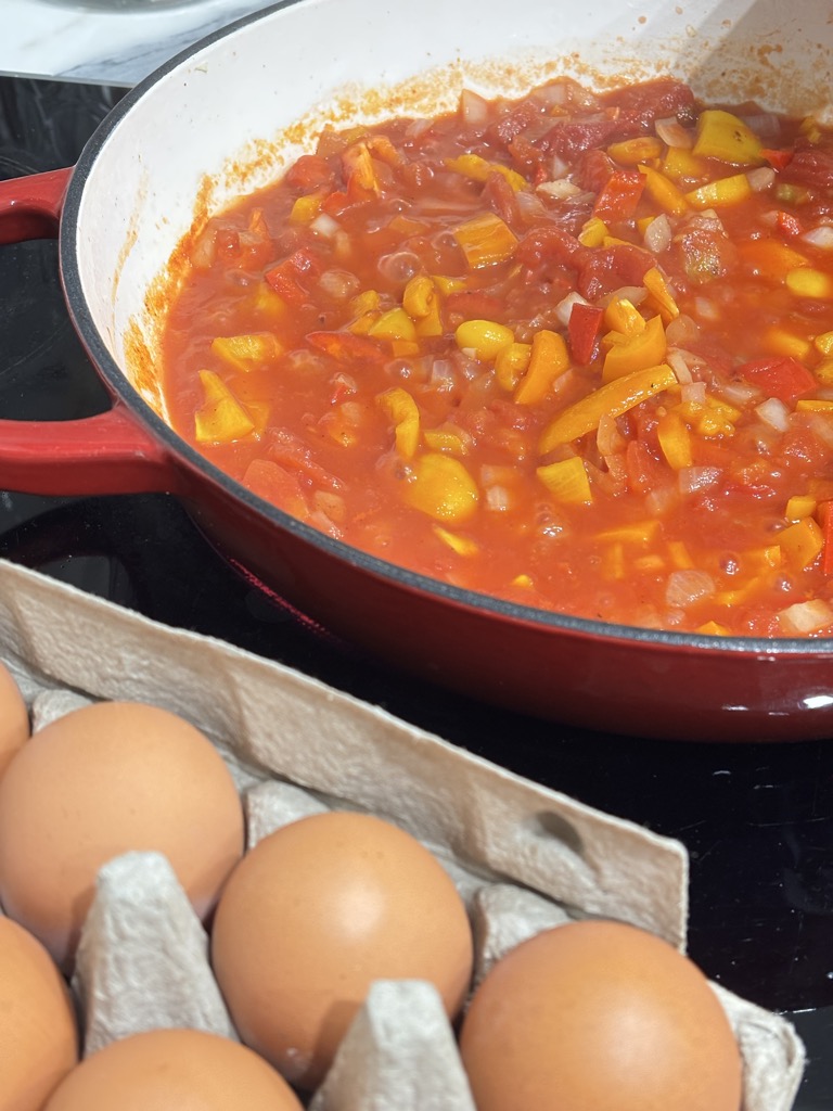 A thick, spicy tomato sauce bubbling in a deep red skillet with yellow and red peppers — the perfect foundation for a classic shakshuka with poached eggs.