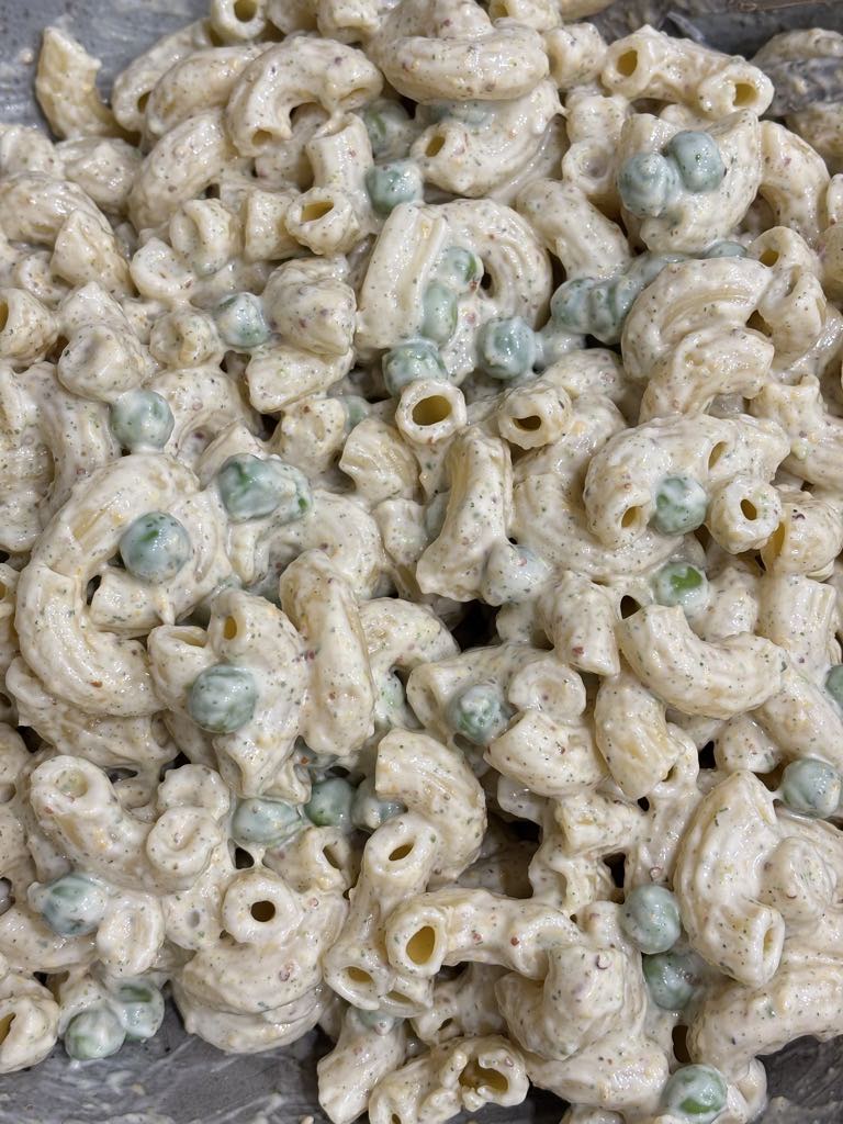 A large bowl filled with elbow macaroni salad coated in a speckled, creamy dressing with peas mixed throughout.