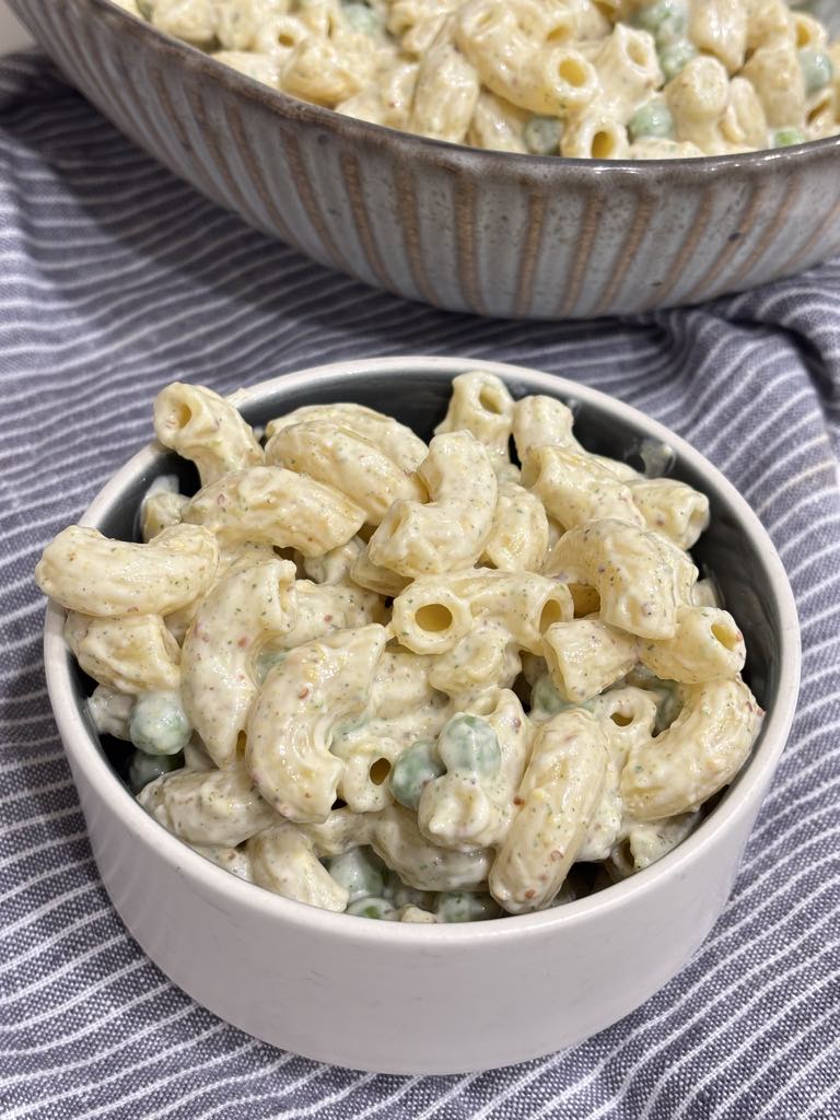 A detailed view of tender elbow macaroni and peas covered in a thick, well-seasoned mayonnaise dressing.
