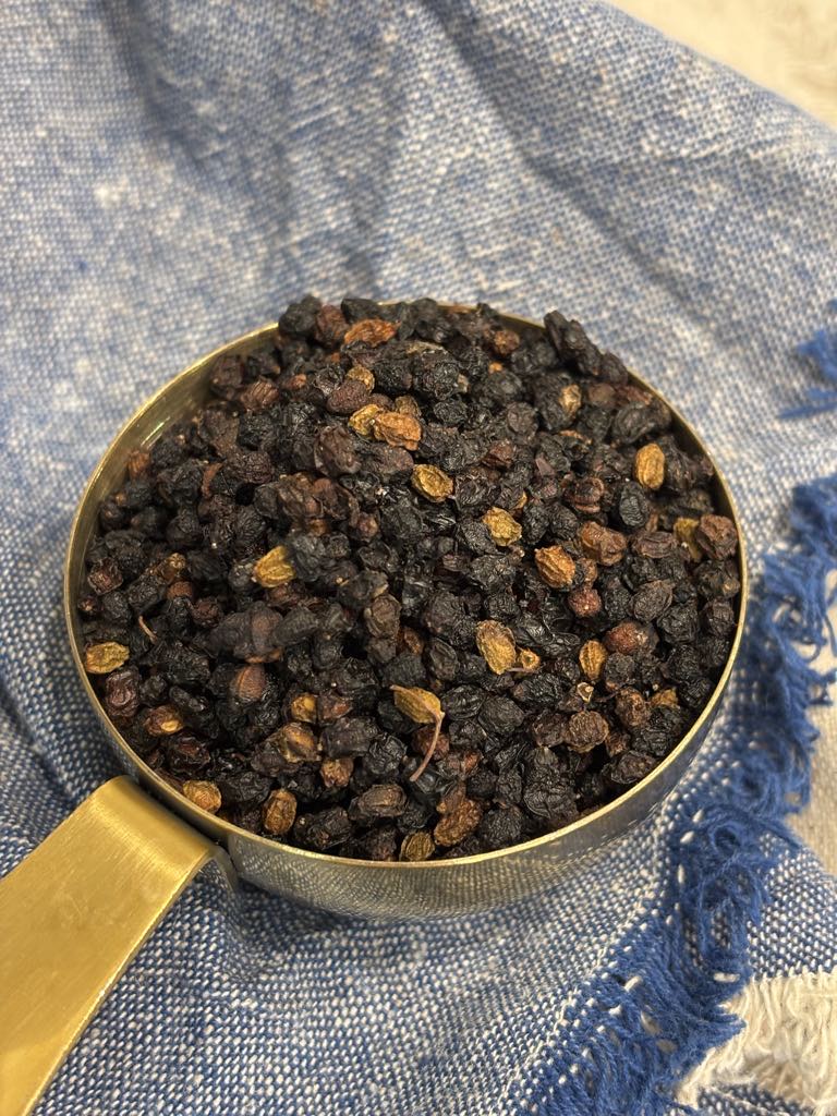 A measuring cup filled with dried black elderberries ready to be used in a traditional homemade elderberry syrup recipe.