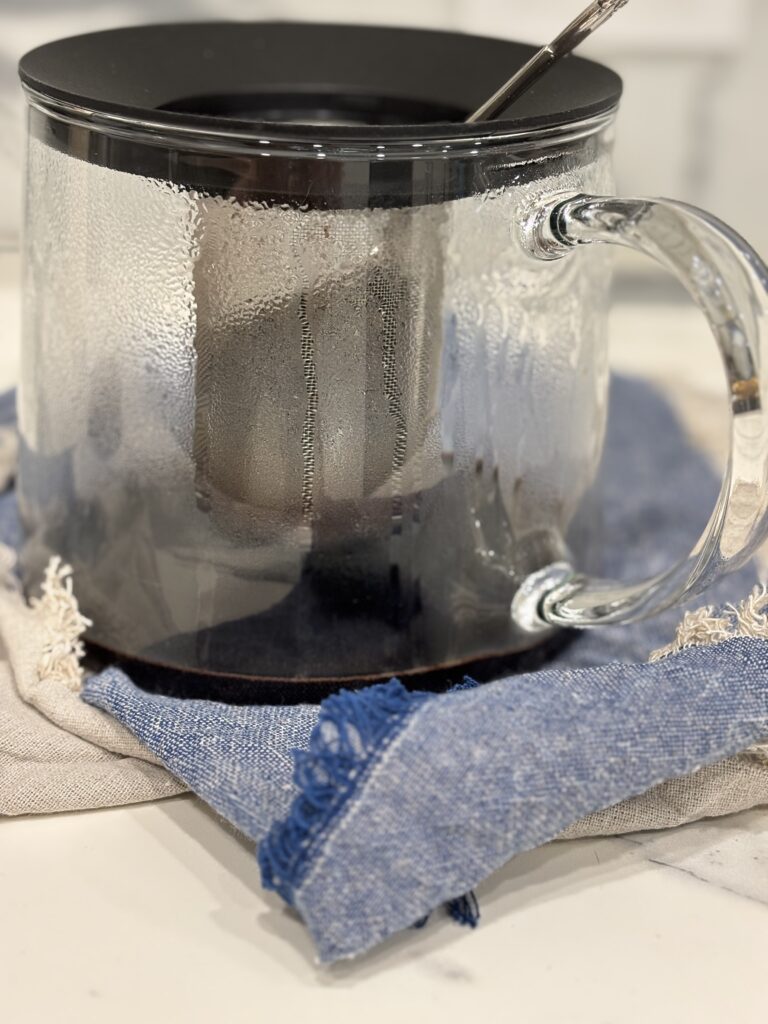 Warm elderberry mixture being strained through a fine mesh strainer to extract rich elderberry juice for homemade elderberry syrup.