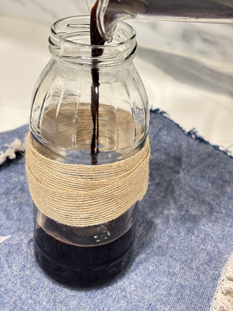 Freshly strained elderberry syrup being carefully poured into a glass jar, ready for honey to be added and stored.