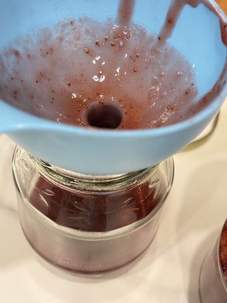 Hot small batch strawberry jam being poured through a funnel into clean jars, an old-fashioned step in making strawberry jam without pectin.