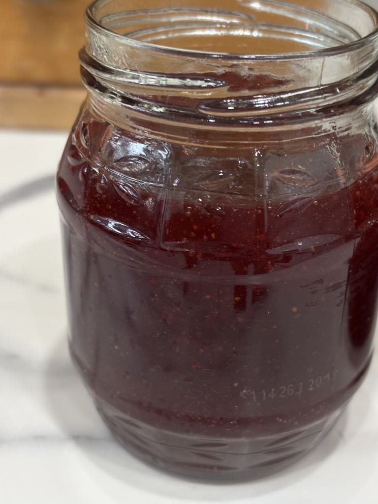 A filled jar of homemade strawberry jam without pectin, cooling at room temperature after cooking using a traditional small batch method.