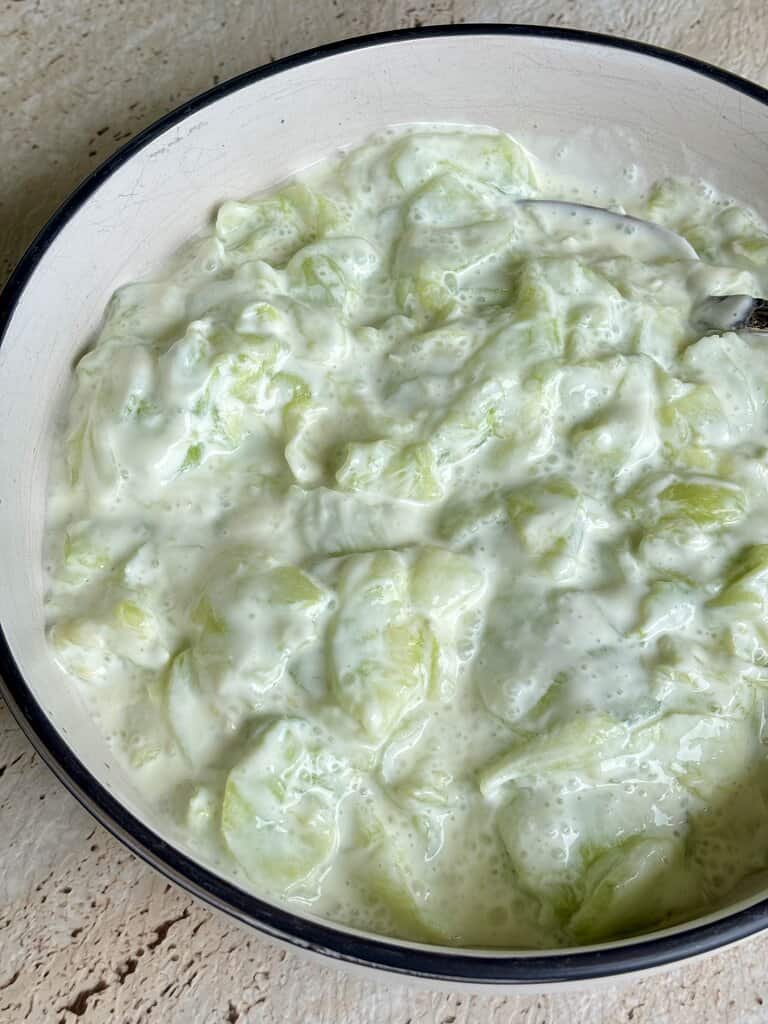 Close up of creamy cucumber salad showing tender cucumber slices in a rich, tangy dressing, ready to serve as a refreshing side dish.