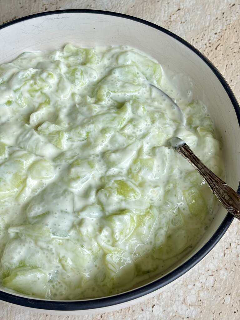Homemade creamy cucumber salad with chunky cucumber pieces mixed in a smooth dressing, photographed in a bowl on a light surface.