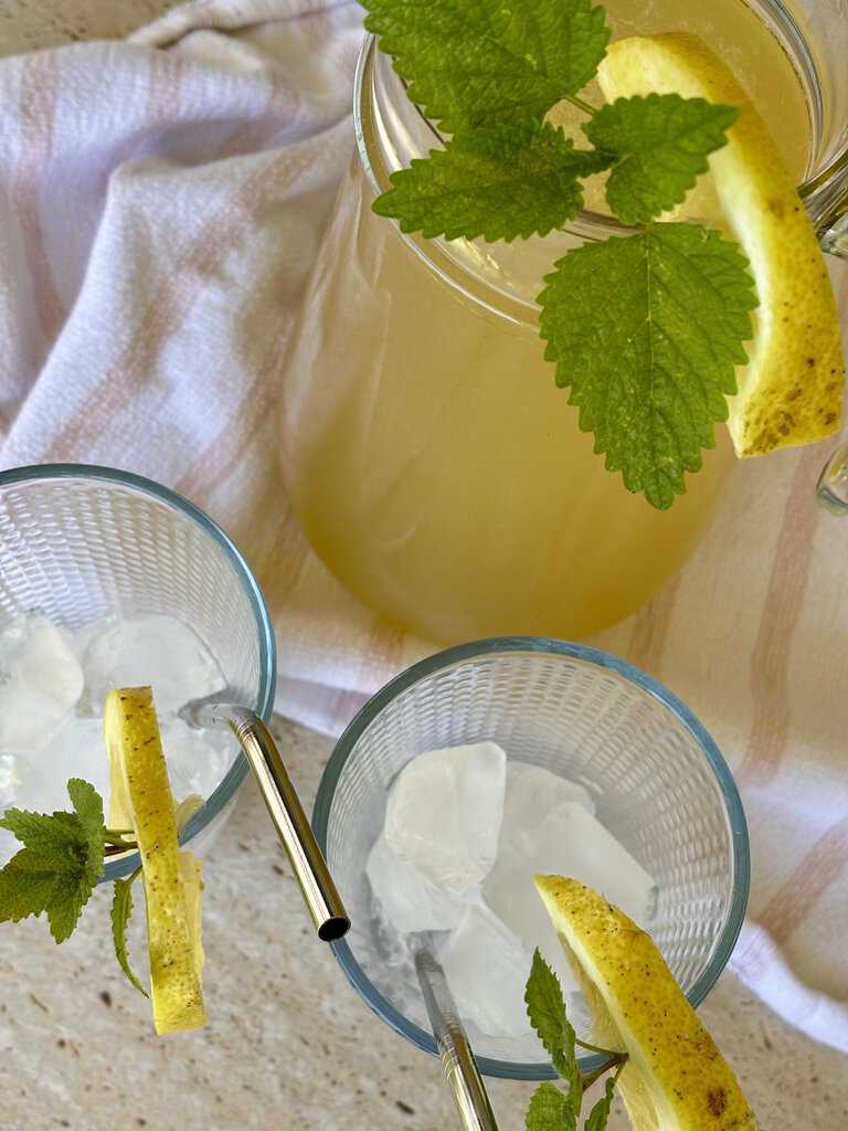 Old-fashioned lemonade recipe served in a clear glass jar with fresh lemon slices and ice cubes on a rustic wooden table.