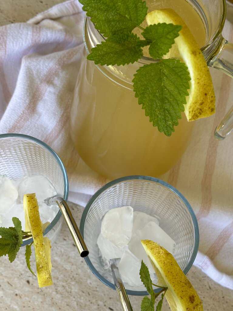 Overhead view of a classic old-fashioned lemonade recipe with whole lemons, a wooden citrus juicer, and glasses of freshly squeezed lemonade.