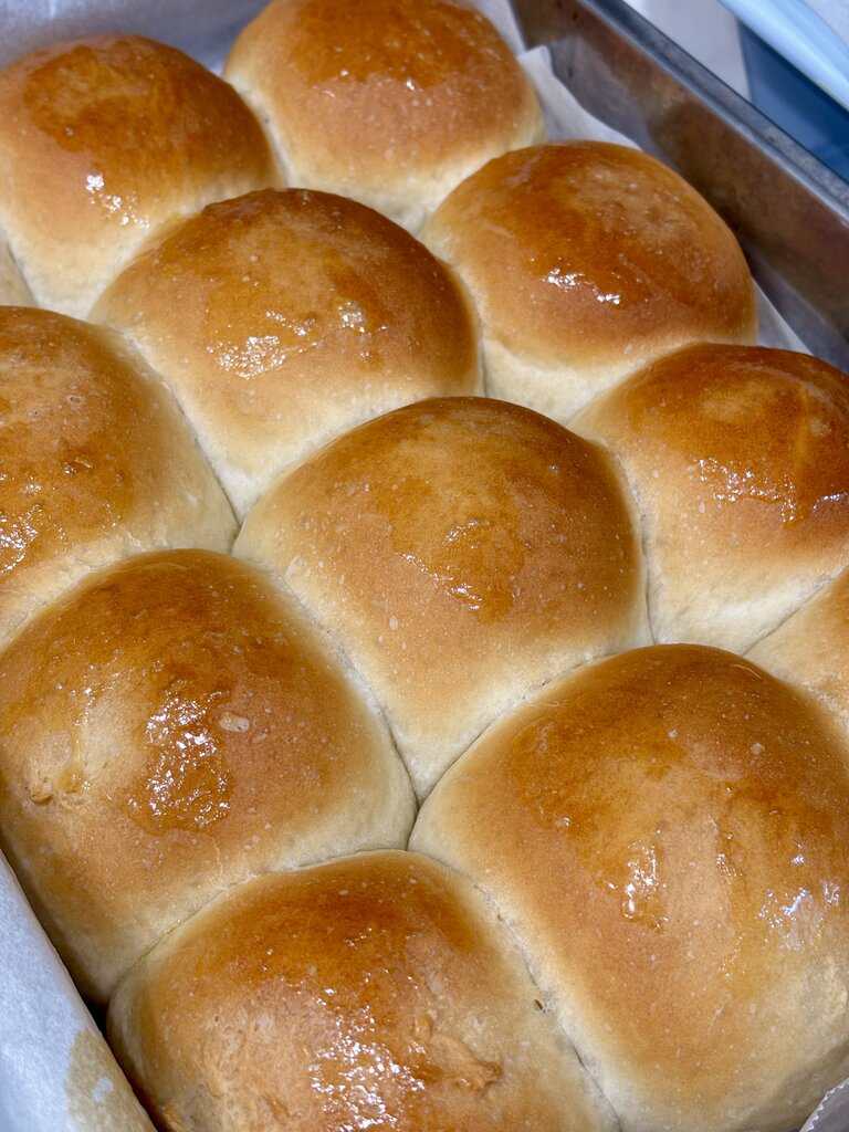 Close up of soft dinner rolls brushed with butter showing smooth golden crust and pillowy shape.