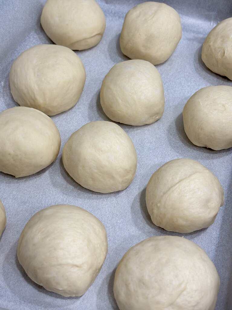 Evenly shaped dinner roll dough balls arranged on parchment paper before proofing.