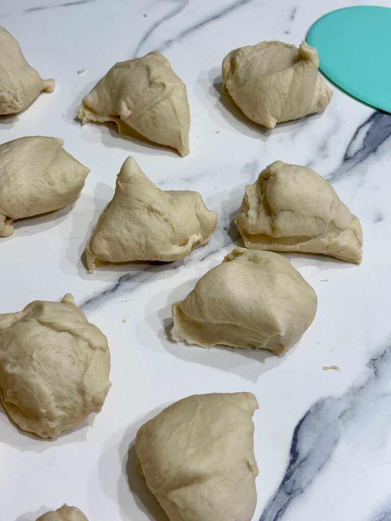 Portioned dough pieces on a countertop ready to be shaped into soft dinner rolls.