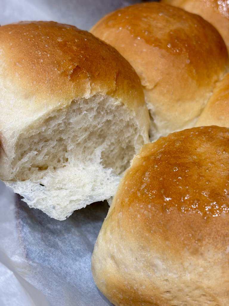 Close up of soft dinner rolls with one pulled apart to show the light, fluffy crumb and golden glossy crust.