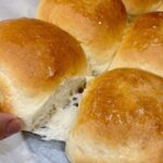Hand pulling apart a soft dinner roll revealing tender, airy texture inside freshly baked rolls.
