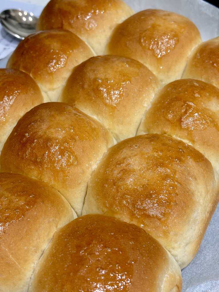 Tray of golden brown soft dinner rolls with shiny tops baked closely together for a pull-apart texture.
